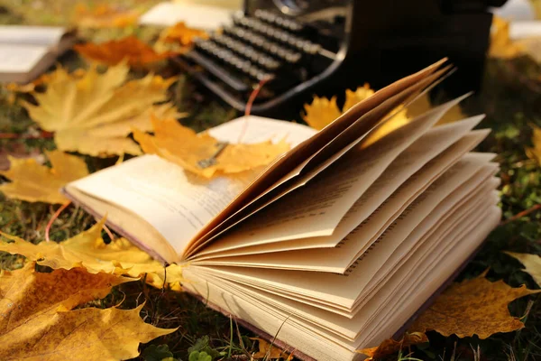 Writing Concept.Autumn Books. retro black typewriter and books with yellow maple leaves on the lawn