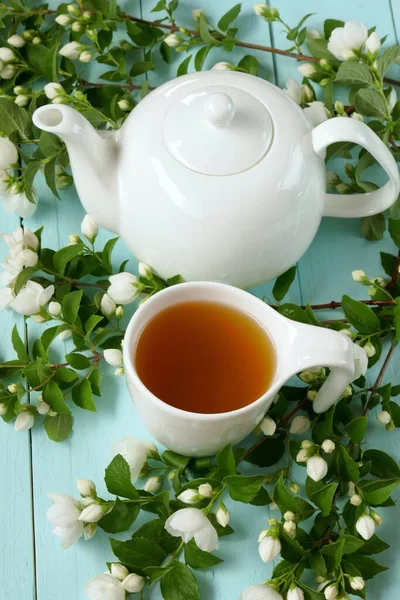 Morning tea Jasmine tea in a white kettle and a cup, a blue alarm clock and a diary and a tray with jasmine branches on a light shabby chic background