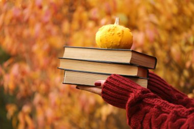 Sonbahar kitapları okuyorum. Bir yığın kitap ve küçük sarı balkabağı.