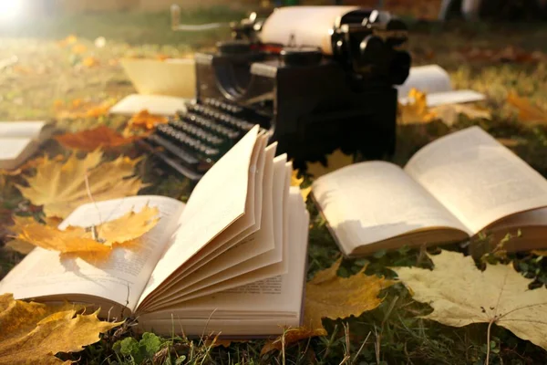 Writing Concept.Autumn Books. retro black typewriter and books with yellow maple leaves on the lawn