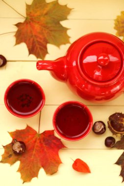 Sonbahar çayı, kırmızı çaydanlık, çay fincanı, akçaağaç yaprağı, kestane, bitki özü. 