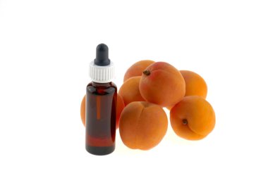 Bir şişe bardakta kayısı yağı pipetli ve taze kayısılı.