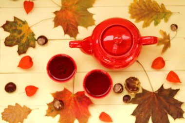Sonbahar çayı, kırmızı çaydanlık, çay fincanı, akçaağaç yaprağı, kestane, bitki özü. 