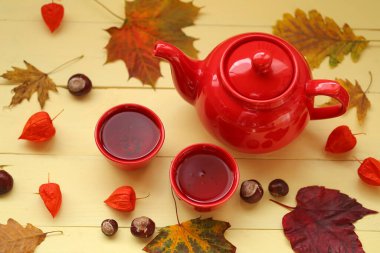 Sonbahar çayı, kırmızı çaydanlık, çay fincanı, akçaağaç yaprağı, kestane, bitki özü. 