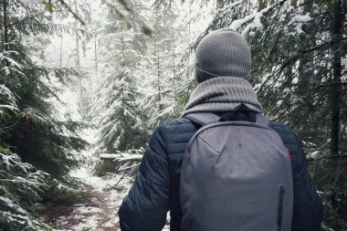 Sırt çantalı adam kışın ormanda yürüyor.