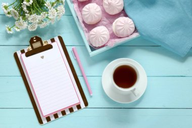 Bahar çayı. Düz yatıyordu. İlkbahar yapılacaklar listesi. Boş bir pano, pembe şekerlemeler, bir fincan çay ve mavi pastel arka planda beyaz bir çaydanlık..