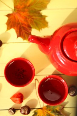 Sonbahar çayı, kırmızı çaydanlık, çay fincanı, akçaağaç yaprağı, kestane, bitki özü. 