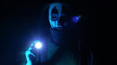 Karanlıktan ürpertici bir bakış. Manyak, fenerli bir kurban arıyor. Korkunç Cadılar Bayramı. Karanlıkta kapüşonlu korkunç bir maske. Çığlık etkisi. 4k görüntü