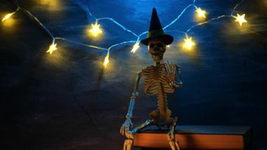 Cadılar Bayramı Kitabı. Keleton, kara tahta üzerine kitap yığını üzerine şapka takıyor. Cadılar Bayramı için ürkütücü hikayeler. 4k görüntü