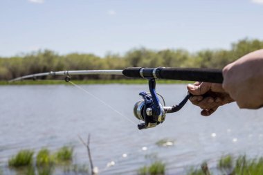 Bir adamın eli oltayı tutar ve makarayı çevirir. Gölde balık avı..