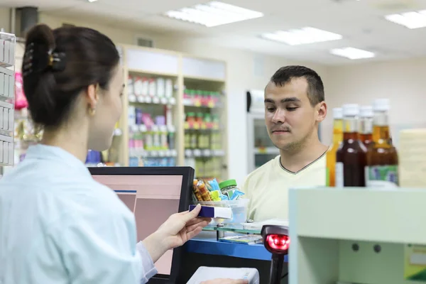 Man buys medicine. Female pharmacist standing at the cash register sells drugs to a man. The pharmacist counts the cost of the drug on the computer.