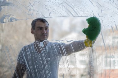 Bir adam evin pencerelerini yıkıyor. Cam temizleme süngeri ile pencereyi yıkamak ve temizlemek. Ev temizliği.