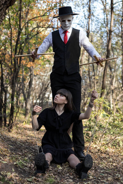 Кукловод в маске контролирует и манипулирует девочкой. Девушка изображает куклу. Концепция манипуляции и контроля. Хэллоуин.