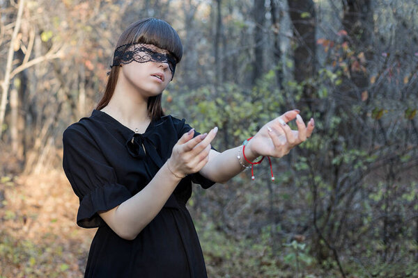 A girl with a blindfold and outstretched arms looking for someone in the woods.Blind girl.