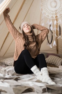 A young woman stretches after sleeping in a teepee. Rest in a wigwam. Awakening. clipart