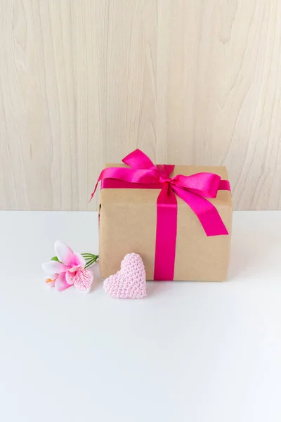 Happy Women\'s Day, Happy Mother\'s Day, Happy Valentine\'s Day and Happy Birthday. A flower, a crochet heart and a beautiful gift wrapped in a pink ribbon. Wooden background and white base. Copy space.