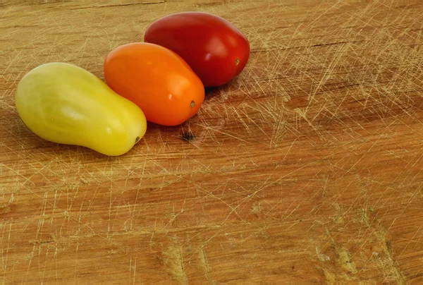 Healthy and shiny cherry tomatoes of different colors on a rustic cutting board. Off-center to leave space for text.