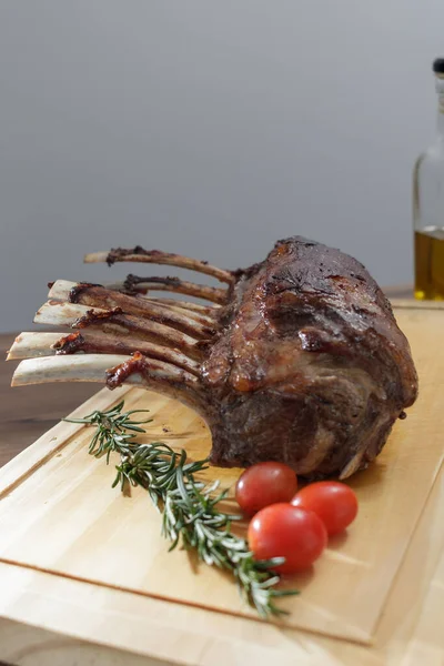 oven-roasted lamb rib with rosemary and olive oil, ready to eat with cherry tomatoes, wooden table and gray background