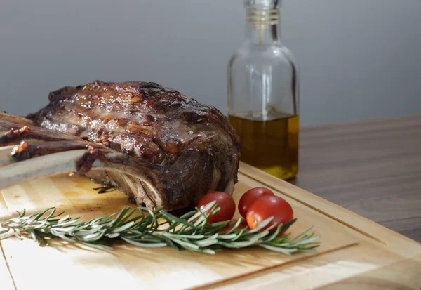 oven-roasted lamb rib with rosemary and olive oil, ready to eat with cherry tomatoes, wooden table and gray background