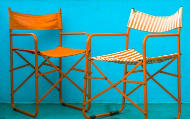 Mavi duvarın üzerinde iki renkli eski çizgili turuncu ve beyaz plaj sandalyesi