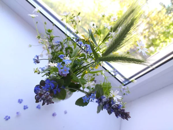 Bunch of wild flowers in a transparent vase on a white windowsill