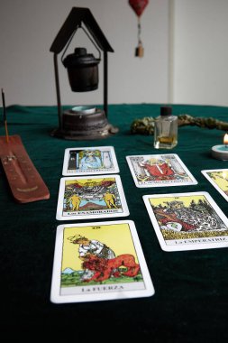 Koyu yeşil kumaş üzerinde tarot kartları, esans şişesi, mum ile adaçayı, tütsü kahverengi masa, altın ay ve beyaz arkaplan ile altın yıldızlar.