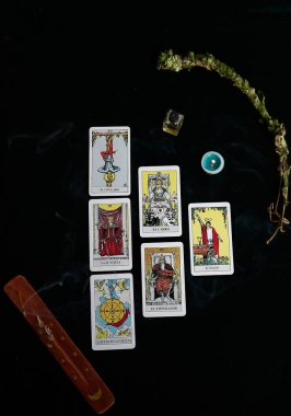 Tarot kartları, esans şişesi, mum ve adaçayı dalı, tütsü kahverengi masa, altın ay ve altın yıldızlar.