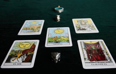 Mumlu tarot kartları ve koyu yeşil kumaş üzerinde iki yüzük.