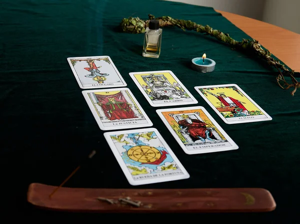 Koyu yeşil kumaş üzerinde tarot kartları, esans şişesi, adaçayı rengi mum, tütsü kahverengi masa, altın ay ve beyaz arkaplanlı altın yıldızlar.