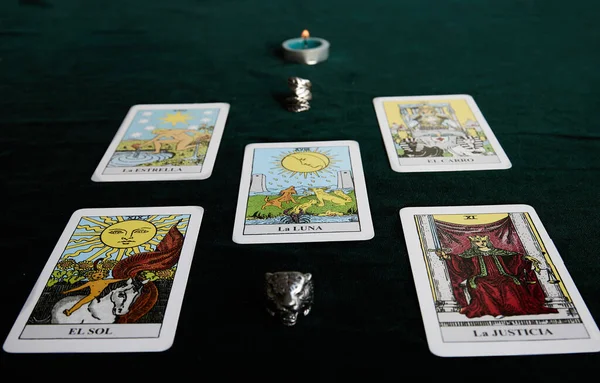 Mumlu tarot kartları ve koyu yeşil kumaş üzerinde iki yüzük.