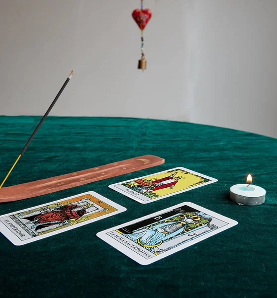 Koyu yeşil kumaş üzerinde tarot kartları kahverengi tütsü masasının yanında altın ay ve beyaz arkaplanlı altın yıldızlar.