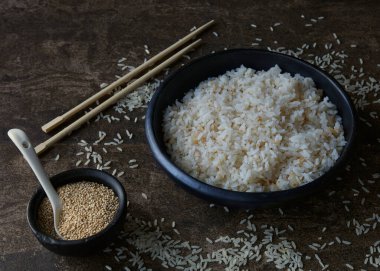 Bir kase pişmiş beyaz pirinç ve üzerinde yemek çubukları olan tohumlar.