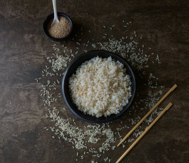 Bir kase pişmiş beyaz pirinç ve üzerinde yemek çubukları olan tohumlar.