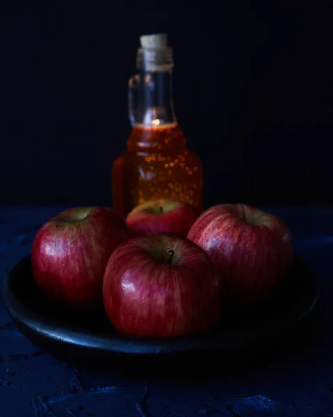 Apples on black plate and a bottle of honey on a blue and black background