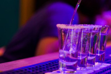 Gece partisinde bar masasında tekila, arka planda insanlar, Tiflis gece kulübünde mavi ışıklı alkollü içkiler..