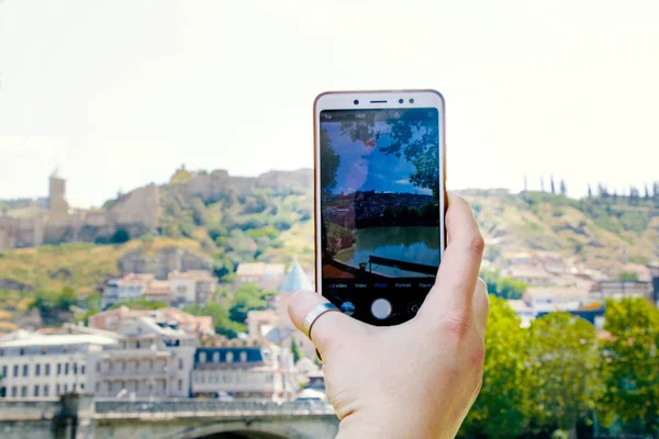 Woman hand and mobile phone, video and photo shooting scene, tourist and traveler take photo and video of old town and city center of Tbilisi, Georgia