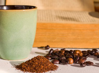 Kavrulmuş kahve çekirdekleri ve taneli kahve çekirdekleri, stüdyo çekimi, kitap ve bardak.