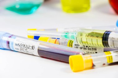 Beyaz arka planda Corona virüsü ve Covid-19 pozitif kan testi tüpleri var. Teşhis ve laboratuvar. Tıbbi iğne ve kan tüpü, korona virüsü veya covid-19 aşısı. Yakın çekim ve stüdyo çekimi.