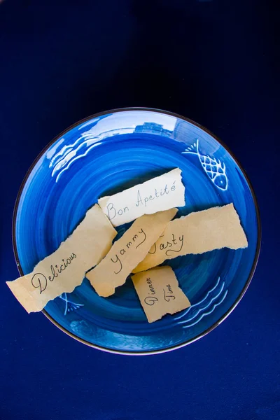 Tasty, delicious, dinner time letters and text, empty blue tableware, bowl and plate on the blue table. Dish set. Table setting.