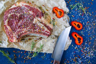 Masada çiğ et, baharatlar ve biberiye, biftek malzemeleri. Biber ve kola tuzu. Doğal ışık.