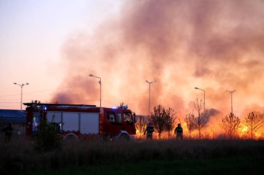 İtfaiyeciler yangınla mücadele akşam takım. İtfaiye arabası alev ve duman arka plan üzerinde.