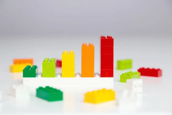 Progress chart made of bricks. Composition of colorful toys on white table.