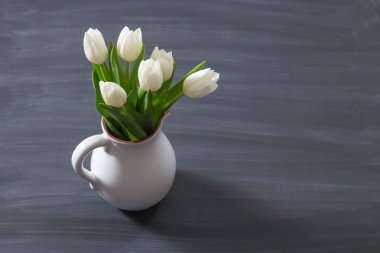 Bir oldfashion rustik vazo tencerede beyaz lale buketi. Kara tahta arka plan üzerinde beyaz sürahi hafif renk çiçek.