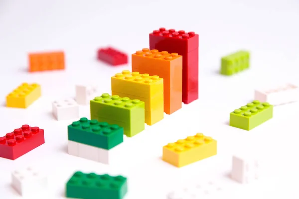 Progress chart made of bricks. Composition of colorful toys on white table.