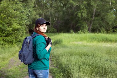 Sırt çantası ve şapkası olan yürüyen bir kız ormanın arka planına doğru döndü.