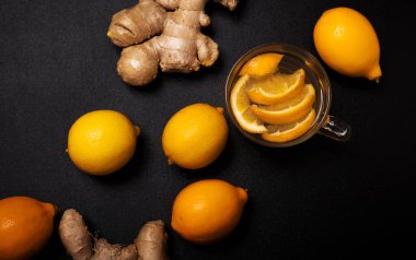 Limon ve zencefil kökleri siyah arka planda bir fincan limon çayı.