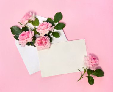 Güzel çiçekler posta zarfında pembe güller ve pembe bir kağıtta yazı için boş bir sayfa. Üst manzara, düz uzanma