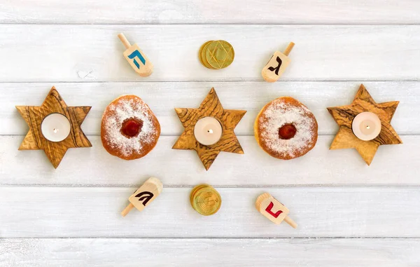 Wooden candlesticks in the shape of star, donut, golden chocolate coins and dreidels on background of white painted wooden planks. Top view, flat lay