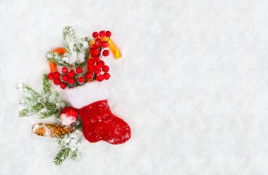 Noel süsü. Yılbaşı çorabı, ağaç dalı, koni, kırmızı böğürtlen, şeker, kardaki kırmızı toplar ve mesaj için yer. Üst manzara, düz uzanma