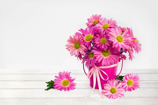 Çiçek buketi pembe kasımpatı papatyaları küçük dekoratif pembe kovada beyaz ahşap bir masa üzerinde kurdele ve metin için boşluk.